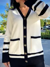 Cardigan de punto en color blanco con detalles en negro en los bordes, cuello en V, cierre frontal con botones dorados y bolsillos delanteros.