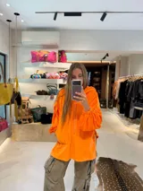 Buzo oversize de plush color naranja, con capucha ajustable por cordones, bolsillo canguro delantero y mangas largas abullonadas con puños elásticos.