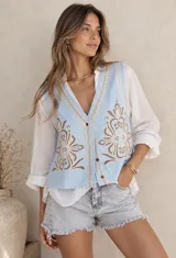 Chaleco celeste con cuello en V, cierre frontal con botones y detalles de bordados florales en tonos beige y marrón.