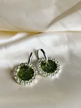 Aros colgantes con forma circular, hechos de resina color lila y borde de strass plateado. El aro es de acero quirúrgico plateado.