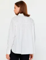 Camisa blanca de manga larga con cuello clásico y cierre frontal de botones. Presenta detalles bordados florales tono sobre tono en la zona de los hombros y el pecho.