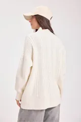 Sweater de punto negro con diseño de trenzas verticales, cuello alto y corte holgado de estilo oversize.