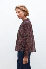 Blusa negra con estampado floral en tonos rosados y rojos, cuello con volados y mangas largas con puños elásticos.