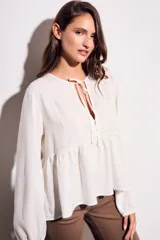 Blusa color crudo de viscosa y lino con bordados en el frente, escote con lazo y mangas largas. Corte holgado con frunce en la cintura.