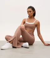 Pantalón deportivo de tiro alto con corte flare, confeccionado en microfibra elástica. Presenta un diseño ajustado en caderas y muslos con una apertura acampanada desde la rodilla y detalle de tajo lateral en el ruedo.