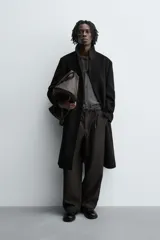 Abrigo negro de corte recto confeccionado en tejido con lana. Tiene cuello alto, manga larga con puños abotonados, bolsillos laterales y abertura en la espalda. Cierre frontal con botones.