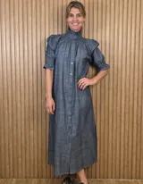 Vestido midi de denim ligero en tono azul, con cuello alto fruncido, cierre frontal abotonado y mangas cortas abullonadas con detalles de nido de abeja en los puños y los hombros.