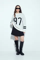 Sweater de punto color blanco con estampado numérico '87' en color negro en el frente y detalles de rayas horizontales en las mangas. Presenta cuello redondo y un corte relajado.