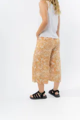 Pantalón de corte culotte y tiro medio, confeccionado en viscosa con estampado de hojas blancas sobre fondo color miel. Presenta una silueta amplia y fluida, con cintura elástica en la parte posterior y bolsillos laterales.