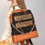 Mochila de cuero vacuno color negro, con detalles en cuero color tabaco y animal print. Tiene dos bolsillos frontales con cierre, correas ajustables y cadena decorativa. El interior está forrado y cuenta con un bolsillo con cierre y otro pequeño para el móvil.