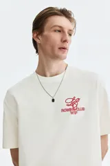 Remera boxy de algodón color blanco, con cuello redondo acanalado, mangas cortas y hombros caídos. Presenta un pequeño estampado rojo en el pecho con las inscripciones 'ROWING CLUB W1F'.