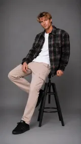 Camisa tipo overshirt de manga larga con diseño a cuadros en tonos oscuros, gris y detalles en naranja. Presenta cuello clásico, cierre frontal con botones y bolsillos en el pecho.