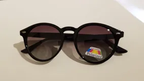 Lentes de sol con montura redonda de plástico negro y lentes polarizados con tinte degradado.