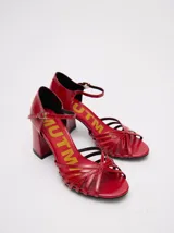 Sandalias de taco alto ancho con diseño retro, confeccionadas en charol negro. Presentan tiras delanteras múltiples entrelazadas, talón cerrado y una correa fina ajustable al tobillo con hebilla metálica.