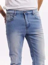 Jean de corte slim fit en color azul claro con lavado localizado. Presenta diseño clásico de cinco bolsillos, cierre frontal con botón y bragueta, y ruedos doblados.