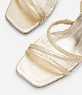 Sandalias doradas de tacón bloque, con tiras finas y cierre de hebilla en el tobillo.