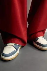 Zapatilla de básquet con cordones, diseño urbano de caña baja. Parte superior confeccionada en combinación de cuero sintético blanco y piezas de denim azul, con suela chunky de goma marrón y entresuela blanca.