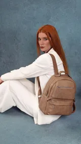 Mochila de cuero sintético en color tostado, con diseño de compartimento principal amplio, bolsillo frontal con cierre y correas ajustables. Presenta herrajes metálicos y asa superior.