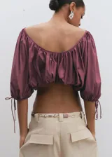 Blusa crop de color bordó, con diseño elástico fruncido, cuello redondo y mangas cortas abullonadas con lazo ajustable en los puños.
