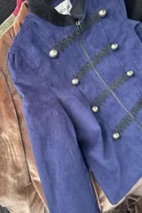 Blazer corto de estilo militar confeccionado en terciopelo azul marino, con cuello mao, cierre frontal con cremallera, detalles de galones bordados y botones metálicos decorativos.