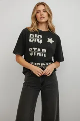 Remera de algodón color negro con efecto lavado, de corte holgado y manga corta. Presenta un estampado frontal con texto y una estrella en tonos claros.