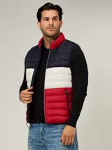 Chaleco acolchado de diseño color block con franjas horizontales en azul marino, blanco y rojo. Presenta cuello alto, cierre frontal de cremallera y dos bolsillos laterales con cierre. Incluye logo de la marca bordado en el pecho.