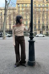 Camiseta color beige de escote recto y hombros descubiertos, con tirantes finos y manga larga. Presenta un detalle de encaje a tono en el escote y está confeccionada en tejido rib.