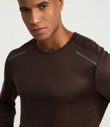 Remera deportiva de manga larga con cuello redondo, confeccionada en tejido técnico Dry Fit. Presenta un diseño liso en color negro con detalles reflectantes en los hombros.