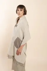 Chal de lana fina sin teñir con diseño a rayas diagonales, presenta un cierre frontal con alamar de fieltro, bolsillos de cuero y terminación con flecos en el ruedo.