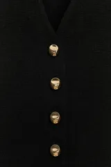 Chaqueta de punto color negro con escote en pico, manga tres cuartos y cierre frontal con botones dorados. Presenta un diseño con bajo asimétrico.