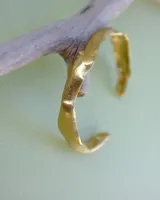 Brazalete rígido abierto de bronce con textura irregular.