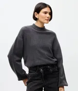 Suéter de punto color gris oscuro, con cuello alto y mangas largas con diseño holgado. Presenta una textura suave y un corte corto.