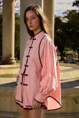 Camisa de algodón color rojo con ribetes negros, cuello mao y cierre frontal con nudos de estilo oriental, mangas abullonadas con puños ajustados.