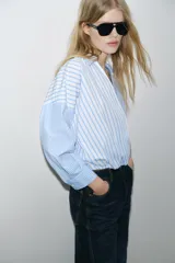 Camisa de popelín con estampado de rayas azules y blancas en diferentes direcciones, cuello solapa, escote pico cruzado, manga larga y bajo elástico.