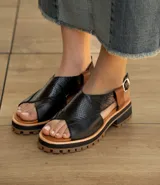 Sandalia de cuero vacuno color negro, con suela de goma deportiva, hebilla al tobillo y horma ancha.