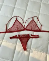 Conjunto de lencería de dos piezas en tul rojo con patrón de corazones y detalles de argollas en forma de corazón. Incluye un bralette triangular con tirantes ajustables y una tanga con la frase "Soy Tuya" aplicada en strass.