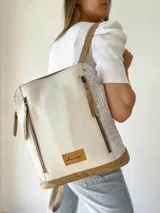 Mochila de cuero color beige y blanco, con detalles laterales texturizados, bolsillos frontales verticales con cierre y asas ajustables.