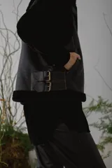 Chaleco de piel sintética en color chocolate, con cierre frontal y detalles de cuero en los bordes. Presenta un diseño de cuello solapa y ajuste lateral con hebillas.