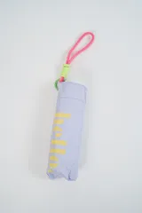 Paraguas plegable de color beige con la palabra 'hello.' estampada en color verde. Incluye una correa de muñeca de color amarillo con detalles en fucsia.