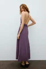 Vestido midi de color morado con cuello halter, tirantes finos ajustables y espalda descubierta. Cuenta con detalles fruncidos en el delantero y la cintura.