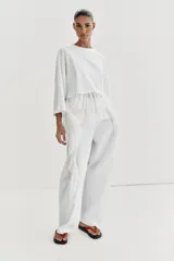 Camiseta de algodón con cuello redondo y manga corta. Presenta un bajo asimétrico confeccionado en un tejido ligero con volantes y una tira lateral decorativa con volantes.