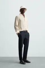 Pantalón chino de algodón color crema, corte regular fit, con cierre frontal de cremallera y botón, bolsillos delanteros y bolsillos traseros de vivo con botón.