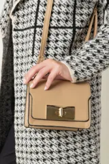 Cartera pequeña color beige, de imitación cuero, con correa larga regulable y asa corta. Presenta un broche metálico dorado en la parte frontal.