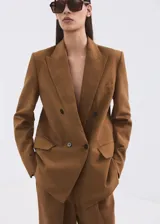 Blazer cruzado de lino y viscosa color marrón tostado, de corte recto y largo, con cuello pico con solapa de muesca, bolsillos laterales con solapa y cierre de doble botonadura.