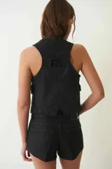 Chaleco de denim con proceso de encuerado, color negro, con escote en V, cierre frontal con botones y bolsillos delanteros con solapa.