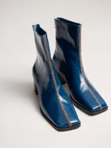 Bota de caña media en cuero negro con punta cuadrada y taco de madera. Cuenta con una costura bordada en color contrastante en el empeine y cierre en la parte trasera.