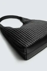 Bolso de hombro tipo hobo o shopper, color negro, con cuerpo de material trenzado. Posee un asa de hombro y un bolsillo interior con cierre de cremallera.