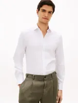 Camisa blanca de corte slim, confeccionada en sarga de mezcla de algodón elástico, con cuello italiano, mangas largas con puño y cierre frontal de botones.