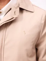 Gabardina de corte clásico en color beige, con cierre frontal de cremallera y botones, cuello camisero y puños ajustables con trabillas.