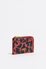 Monedero de estructura rígida con acabado brillante, cierre de cremallera y logo metálico frontal. Presenta un diseño de animal print en tonos rojos y negros.